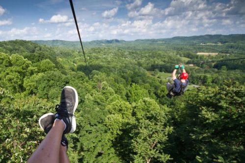 A person zip-lining over a lush green landscape, with one foot visible in the foreground.