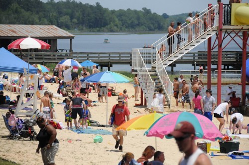 A busy beach scene with people sunbathing, swimming, and enjoying the water, surrounded by umbrellas and a playground.