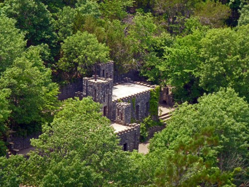 Aerial view of stone ruins surrounded by lush green trees in a forested area.