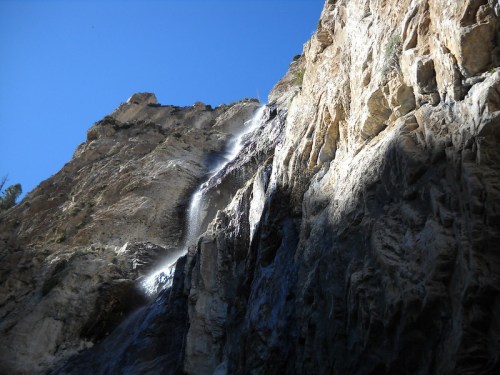 A waterfall cascading down a rocky cliff under a clear blue sky.