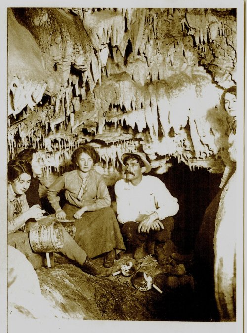 Four people sit in a cave, surrounded by stalactites and stalagmites, engaged in various activities.