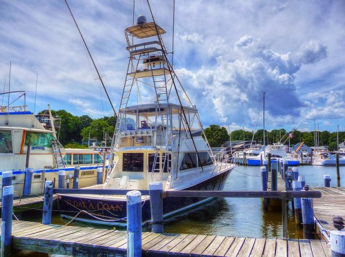 A large fishing boat docked at a marina, surrounded by other boats and under a partly cloudy sky.