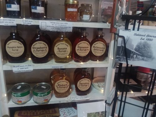 A shelf displaying various flavored syrups in glass bottles, alongside canned goods and a historical photo.