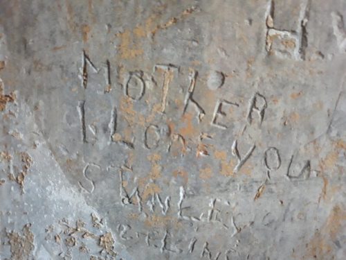 Carved inscription on a metal surface reading "MOTHER I LOVE YOU" with additional markings.