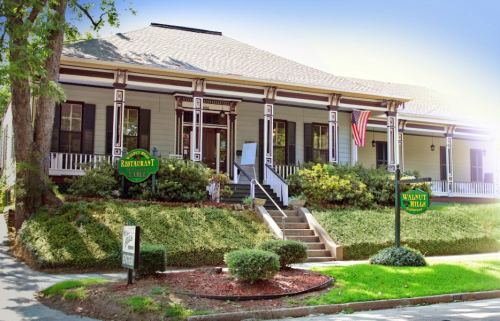 A charming restaurant building with a porch, surrounded by greenery and signs for "Restaurant Table" and "Walnut Hills."