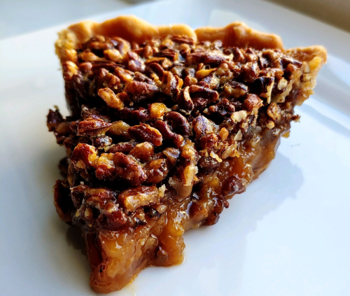 A slice of pecan pie with a golden crust and a rich, nutty filling, served on a white plate.