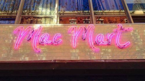 Neon sign reading "Mac Mart" in pink against a reflective window backdrop.