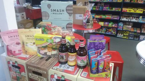 A colorful display of snacks and drinks, including Smash Mallow, candy, and bottles of soda on red tables.