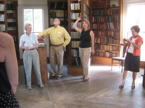 A group of four people in a library, two standing and two taking photos, surrounded by bookshelves.