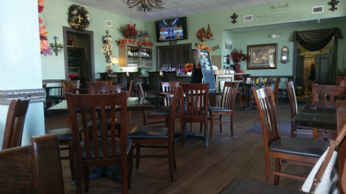Interior of a restaurant with wooden chairs, tables, and seasonal decorations, featuring a bar area and a TV.