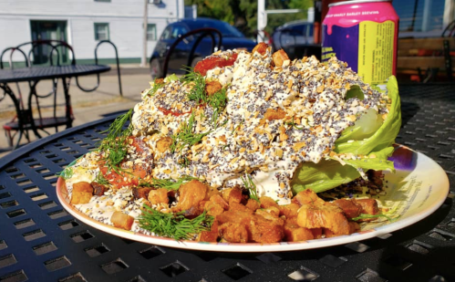 A large salad on a plate, topped with creamy dressing, herbs, and croutons, served outdoors on a sunny day.