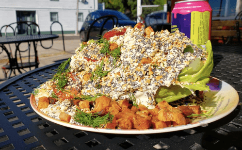 A large salad on a plate, topped with creamy dressing, herbs, and croutons, served outdoors on a sunny day.