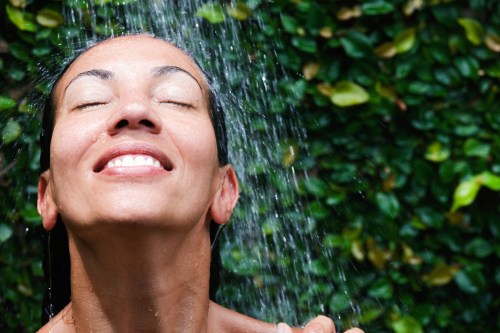 A woman with closed eyes smiles as water cascades over her face, surrounded by lush green foliage.