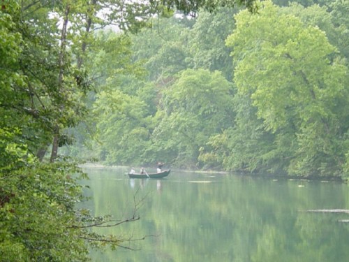 A serene river scene with a small boat and people surrounded by lush green trees and calm water.
