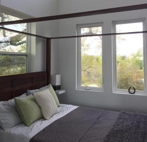 A cozy bedroom with a four-poster bed, green and gray pillows, and large windows letting in natural light.