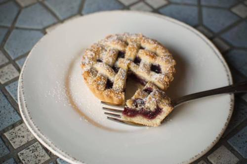 A round fruit tart with a lattice crust, dusted with powdered sugar, on a plate with a fork and a slice cut out.