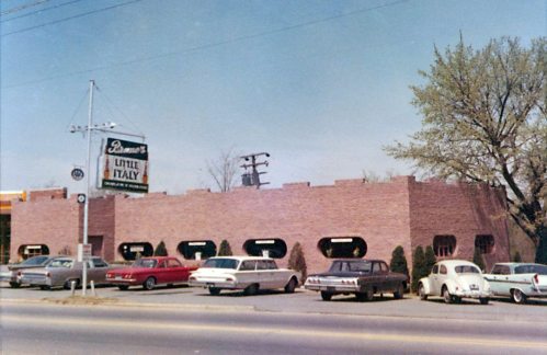 A brick restaurant building with a sign reading "Little Italy," surrounded by parked vintage cars and trees.