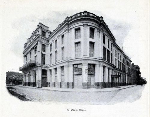 Historic black-and-white image of a grand opera house building, showcasing its architectural details and corner view.