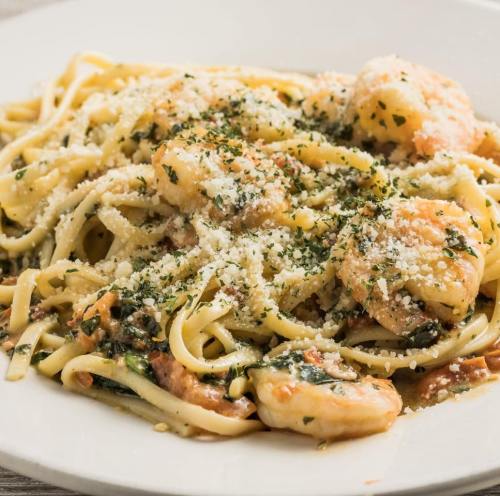 A plate of linguine pasta topped with shrimp, herbs, and grated cheese, served in a creamy sauce.