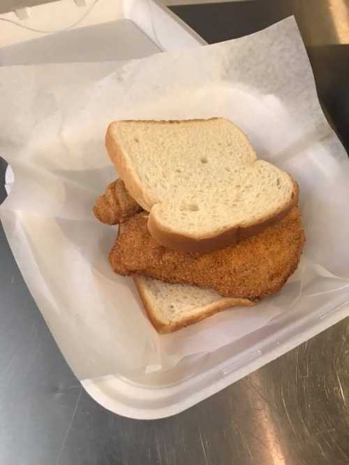 A piece of fried fish sandwiched between two slices of white bread on a paper-lined tray.