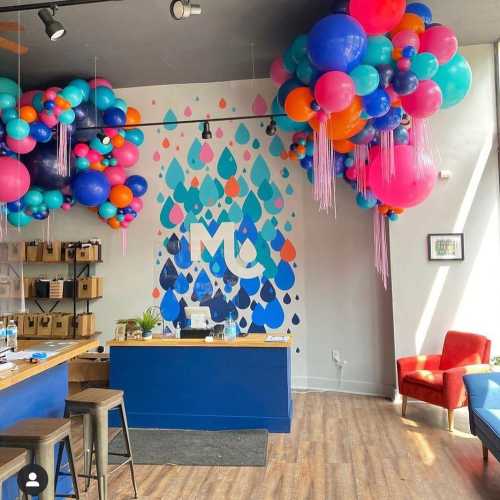 Colorful balloon decorations in a modern space with a blue reception desk and a mural featuring raindrop designs.