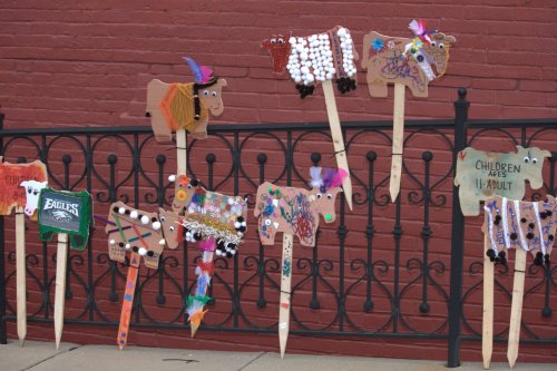Colorful, decorated wooden cow cutouts on sticks displayed against a black fence.