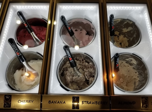 Four ice cream tubs labeled cherry, banana, strawberry, and almond, each with a scoop and a metal ice cream scoop.