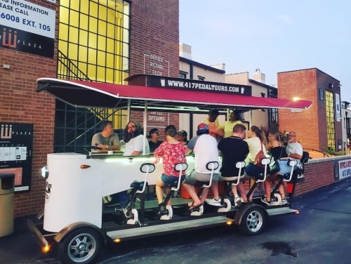 A group of people enjoying a pedal-powered tour vehicle outside a brick building.
