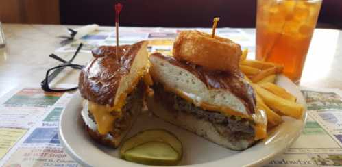 A plate featuring a sandwich with cheese, a crispy potato ball, fries, and a pickle slice, with iced tea in the background.