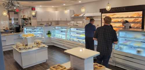 A bright bakery interior with display cases filled with pastries and donuts, and customers browsing the selection.