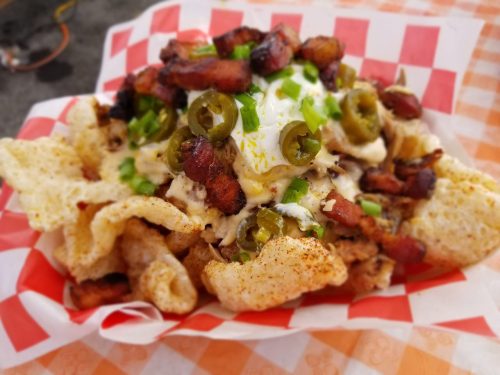 A colorful plate of nachos topped with bacon, jalapeños, green onions, and a dollop of sour cream on crispy chips.