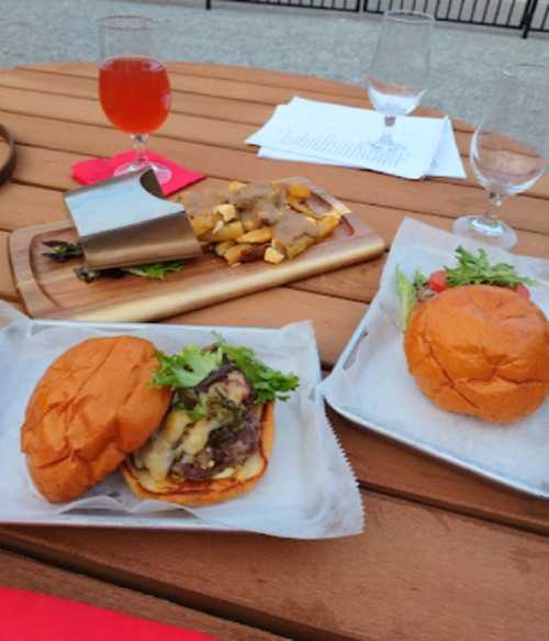 A table with two burgers, one topped with greens, and a plate of fries with gravy, alongside a drink in a glass.