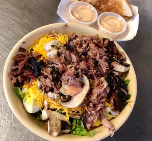 A hearty salad topped with shredded meat, cheese, mushrooms, and served with two cups of dressing on the side.