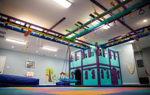 Colorful indoor play area featuring a multi-level play structure, swings, and climbing equipment.