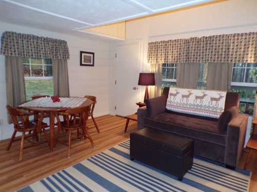 Cozy living space with a sofa, dining table, and patterned curtains, featuring wooden floors and a warm atmosphere.