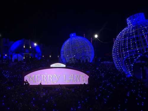 A festive sign reading "Merry Lane" surrounded by large blue ornaments and twinkling lights at night.