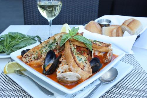 A seafood dish with mussels, clams, and toasted bread, garnished with basil, served with a glass of white wine.
