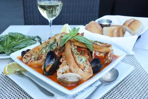 A seafood dish with mussels, clams, and toasted bread, garnished with basil, served with a glass of white wine.