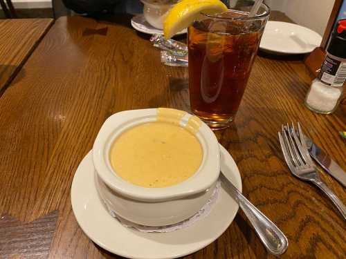 A bowl of creamy soup on a plate next to a glass of iced tea with a lemon slice.