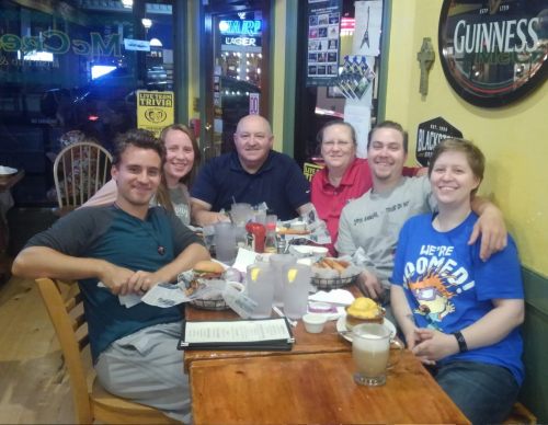A group of six people sitting at a restaurant table, enjoying food and drinks, smiling and chatting together.