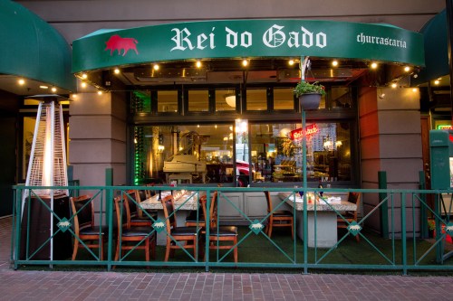 Exterior of "Rei do Gado" churrascaria, featuring green awnings, outdoor seating, and a welcoming atmosphere.