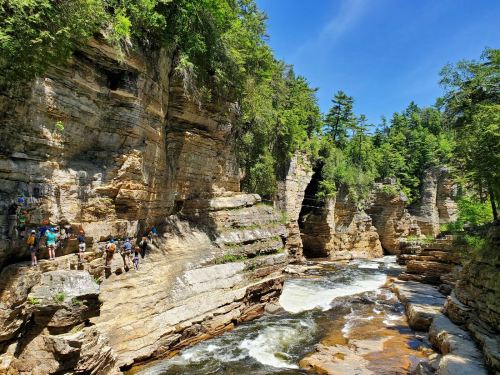 A scenic river flows through rocky cliffs, with people exploring the area under a clear blue sky.
