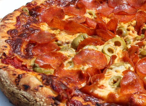 Close-up of a pepperoni pizza topped with green olives and melted cheese, featuring a crispy crust.