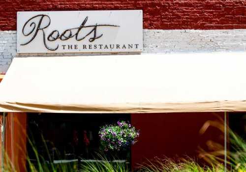 Sign for "Roots The Restaurant" with a beige awning and greenery in front.