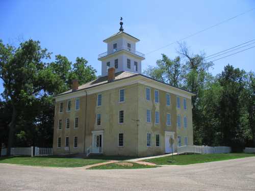 Historic building with a tall cupola, surrounded by trees and a clear blue sky.