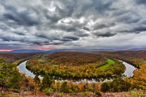 A winding river flows through a colorful autumn landscape under a dramatic, cloudy sky.