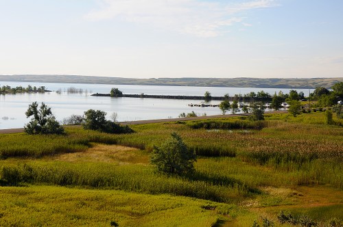 A serene landscape featuring a calm lake, lush green fields, and distant hills under a clear blue sky.