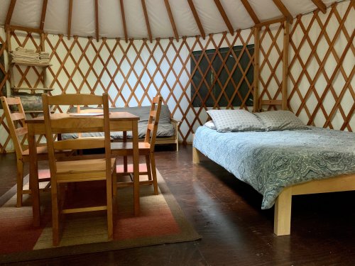 Interior of a yurt featuring a bed, dining table, and chairs, with wooden lattice walls and a cozy atmosphere.