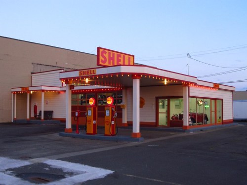 A vintage Shell gas station with bright signage and retro design, featuring fuel pumps and a welcoming facade.