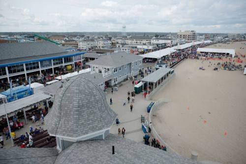 Aerial view of a beach boardwalk with shops, people, and sandy areas under a cloudy sky.